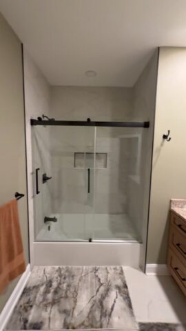 Bathroom renovation in Portsmouth VA featuring frameless glass shower doors, marble-look tile walls and built-in niche